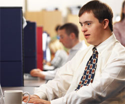 young man with Down Syndrome, working at a desk with a cup of coffee next to his keyboard
