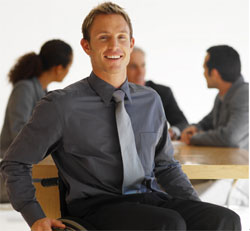 Businessman in a wheelchair smiling, colleagues in background.