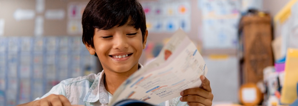 Portrait of elementary boy reading a book in a class.