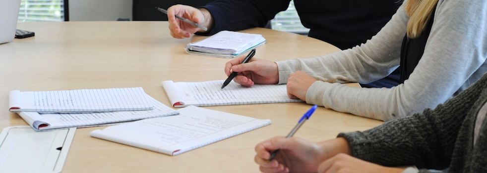 Paper on a desk with three people writing and reviewing