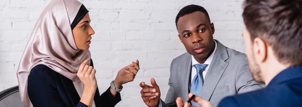 multicultural businesspeople gesturing while discussing contract near interpreter, blurred foreground