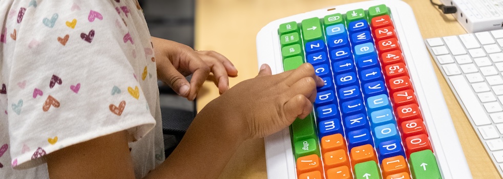 Child typing on a colorful computer keyboard