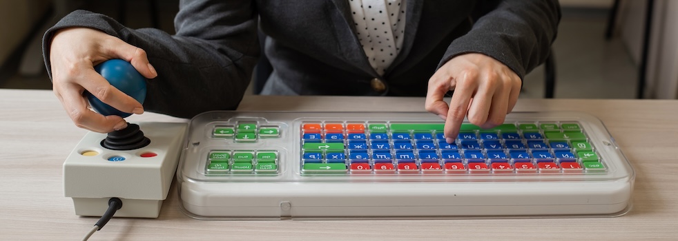 An unrecognizable woman with cerebral palsy is typing on the keyboard. A girl with disabilities works on a specially equipped computer.